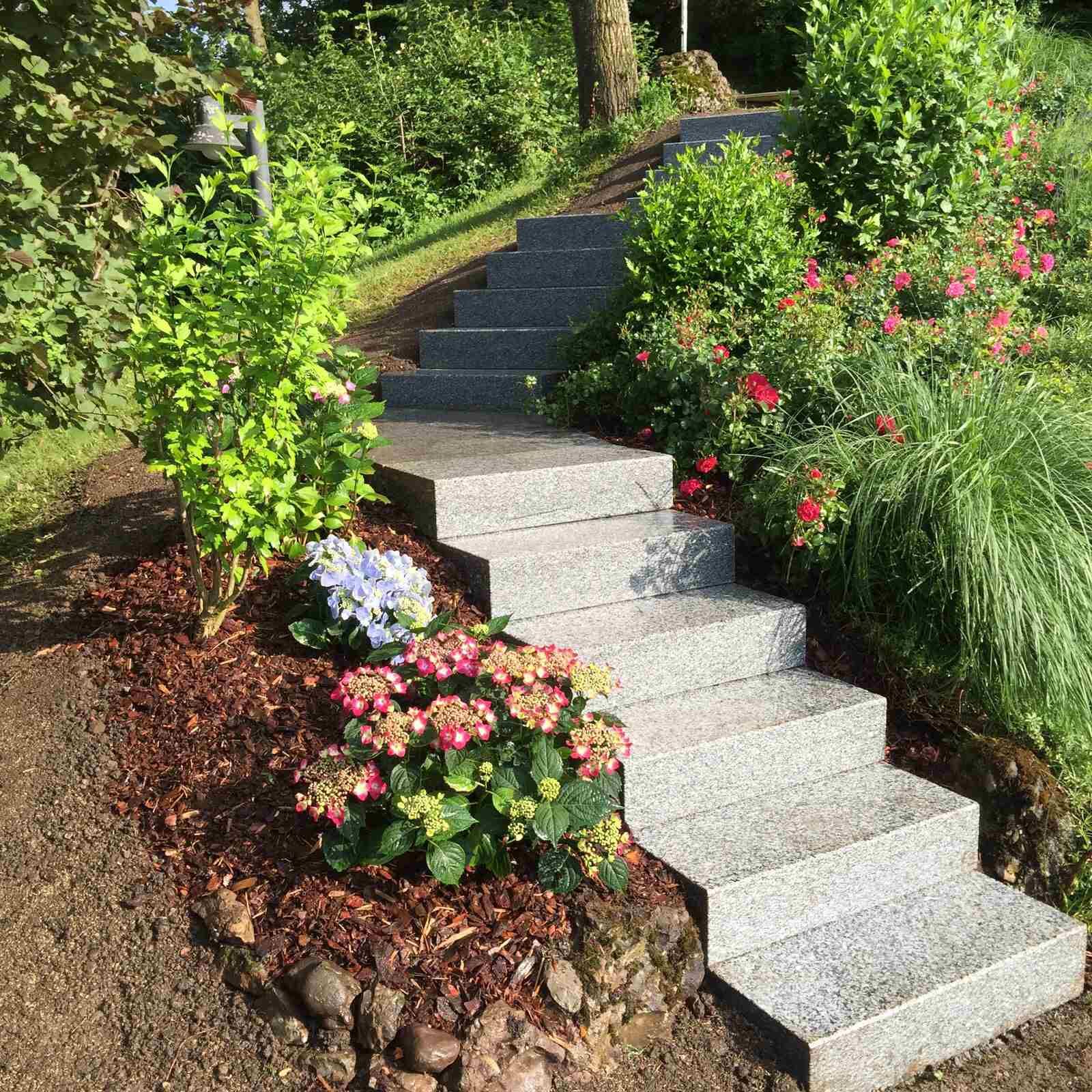 Steinstufen führen einen Gartenhang hinauf, umgeben von Blumen und Grün.