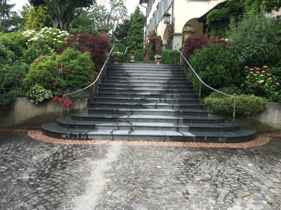 Steintreppen führen zu einem Gebäude hinauf, das von üppigen, vom Regen nassen, grünen Gärten umgeben ist.