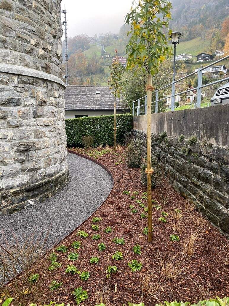 Steinecke mit einem angelegten Gartenbeet und einem Baum. Brauner Mulch und Laub.