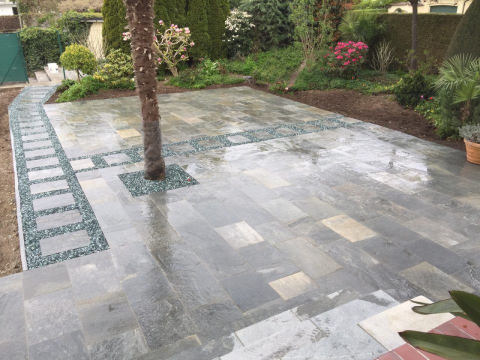 Steinterrasse mit Baum, Weg und Gartengestaltung; Grau- und Grüntöne.