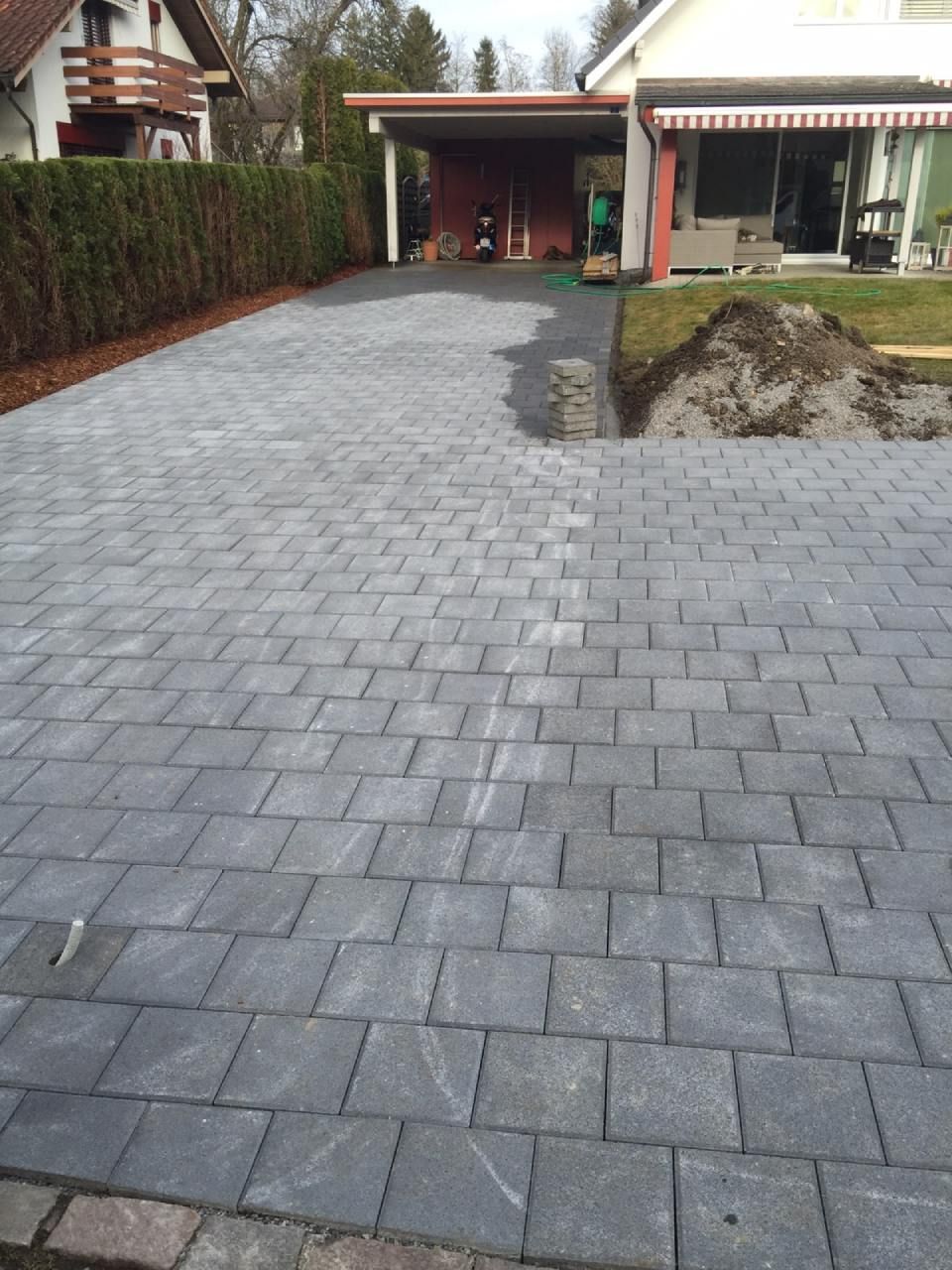 Eine graue Ziegelsteinauffahrt führt zu einem Carport und dem Haus; die Landschaftsgestaltung ist im Gange.