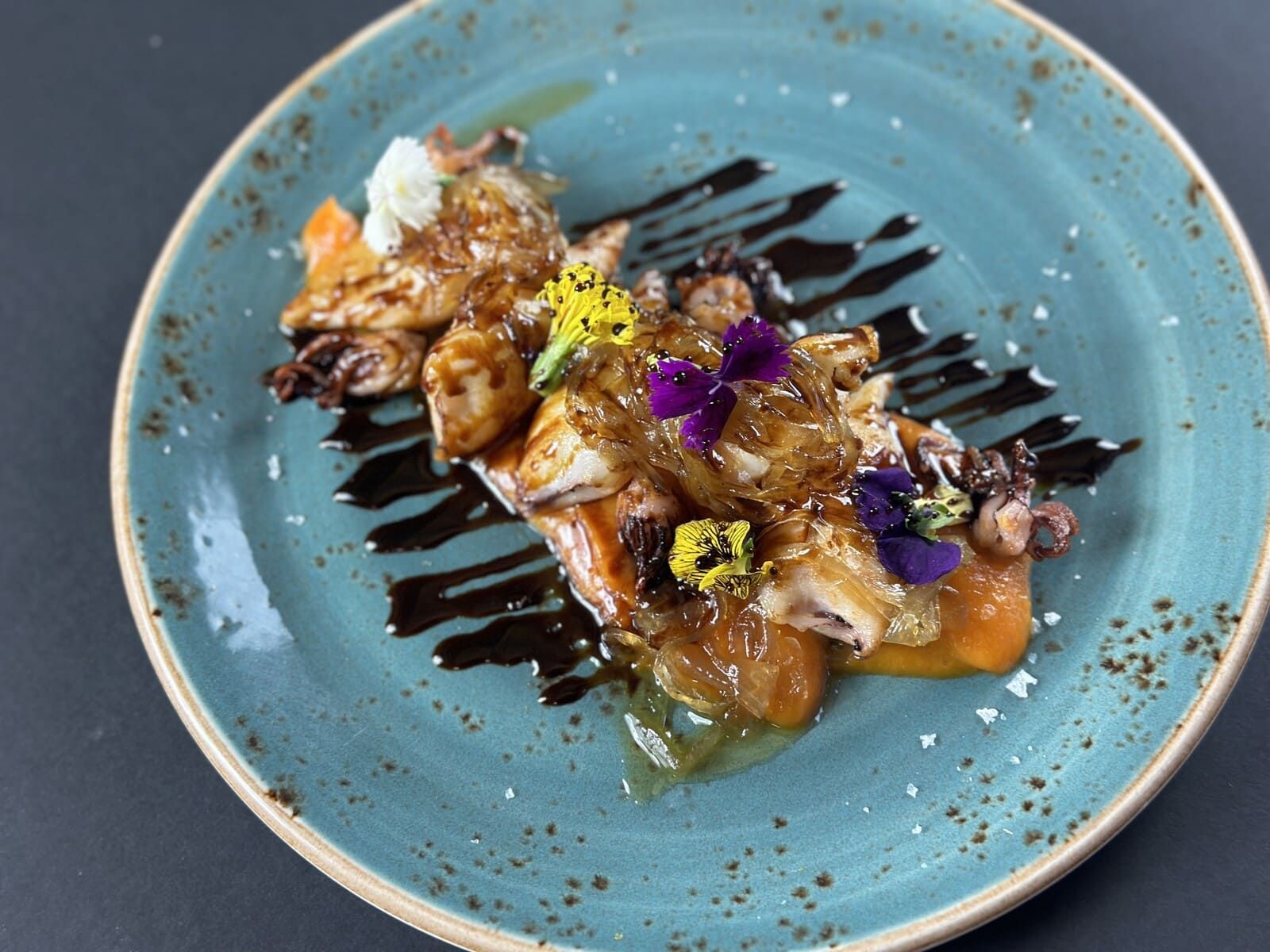 Un plato azul cubierto con comida y flores sobre una mesa.