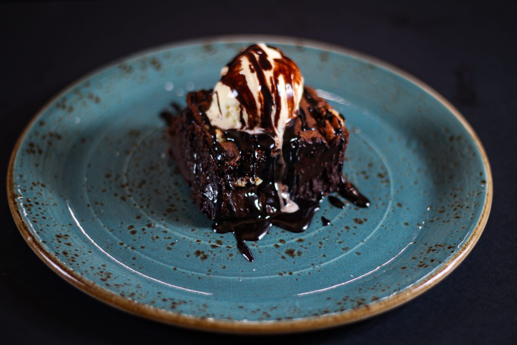 Un brownie con helado y salsa de chocolate en un plato azul.