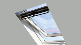 Claraboya abierta con marco blanco, en ángulo sobre un fondo gris. Tirador negro. Cielo azul visible a través del cristal.