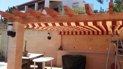 Pérgola con toldo de rayas rojas y blancas sobre zona de comedor exterior.