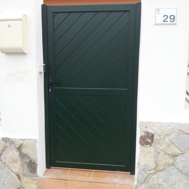 Puerta verde con líneas diagonales, junto a un buzón blanco y el número de casa 29.