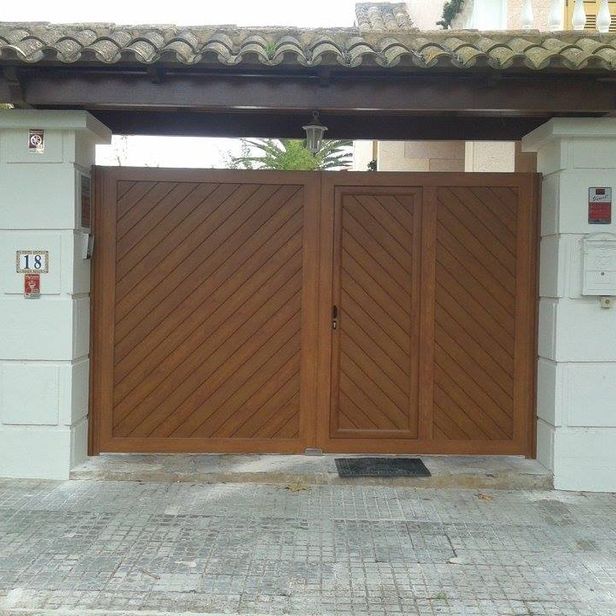 Portón de madera marrón con diseño diagonal frente a una casa, camino de entrada de ladrillo.