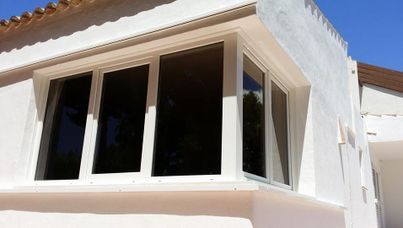 Ventanales con marco blanco en una esquina de un edificio blanco con vidrios polarizados oscuros.