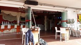 Bar al aire libre con paredes rojas, sillas blancas y entrada parcialmente abierta.
