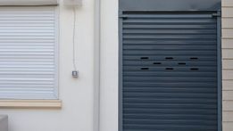 Puerta enrollable gris y ventana blanca con persiana en el exterior del edificio.