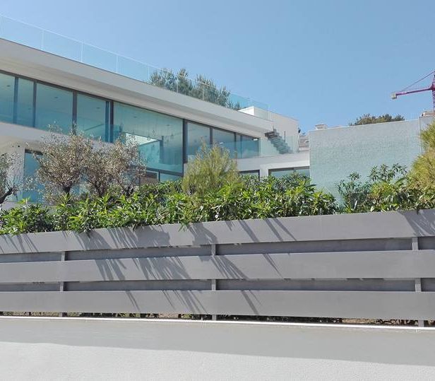 Casa blanca moderna con grandes ventanales de cristal y valla gris.