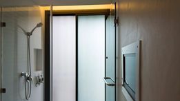 Ducha con puertas de cristal y puerta corrediza esmerilada, accesorios de ducha, TV en la pared.