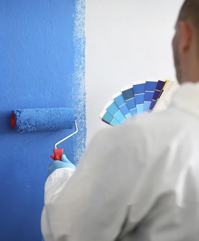 Un hombre está pintando una pared de azul mientras sostiene una paleta de colores.