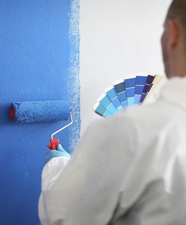 Un hombre está pintando una pared de azul mientras sostiene una paleta de colores.