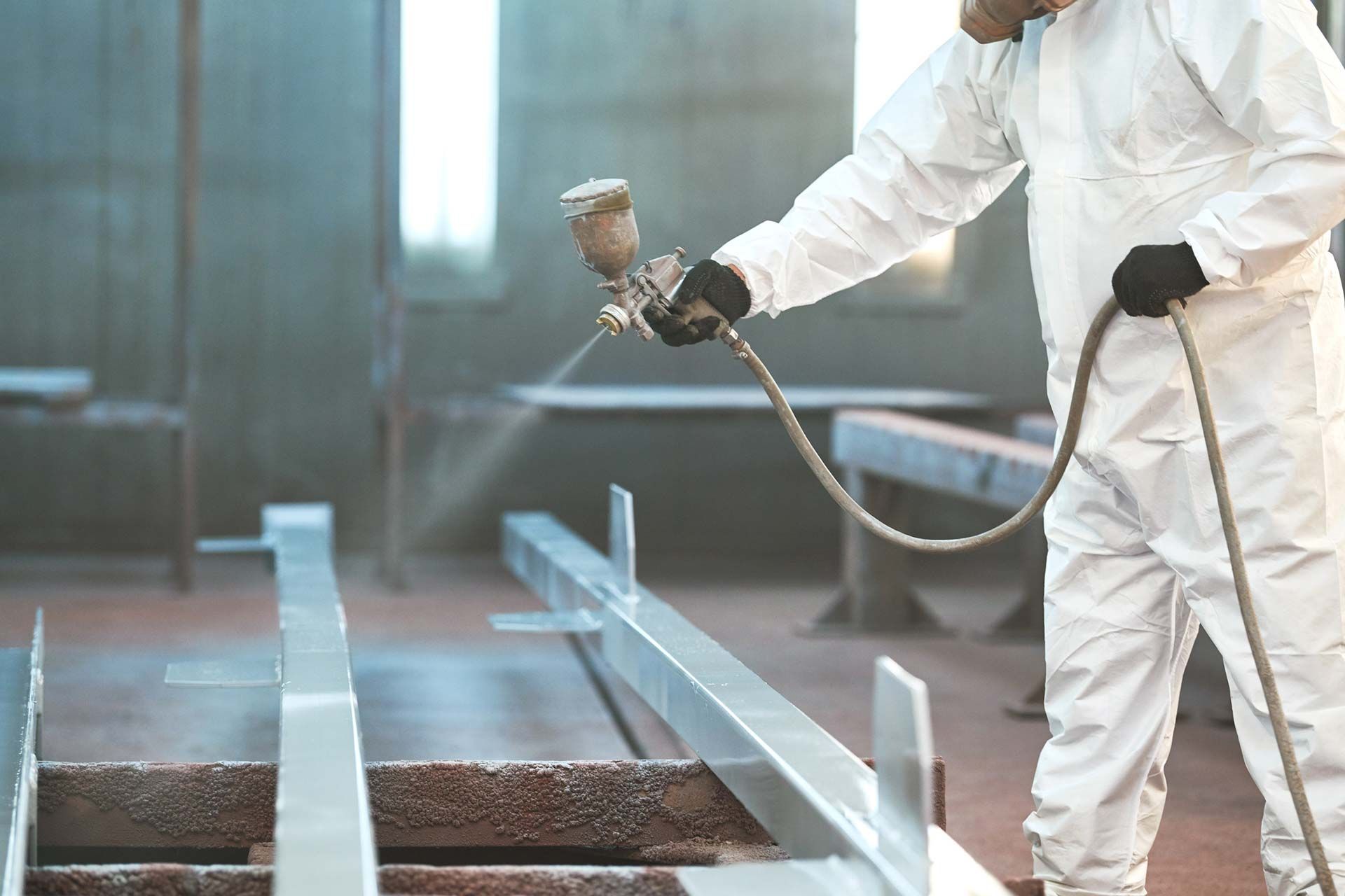 Un hombre con un traje de protección está pintando con aerosol una estructura de metal.