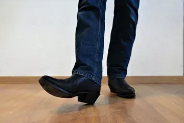 Une personne portant des bottes de cow-boy et un jean se tient debout sur un plancher en bois.