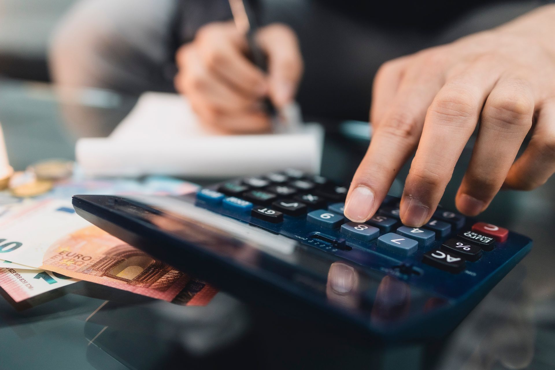 Eine Person benutzt einen Taschenrechner, während sie auf ein Stück Papier schreibt.