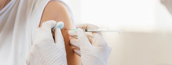 Des mains gantées administrent une injection dans le haut du bras d'une personne