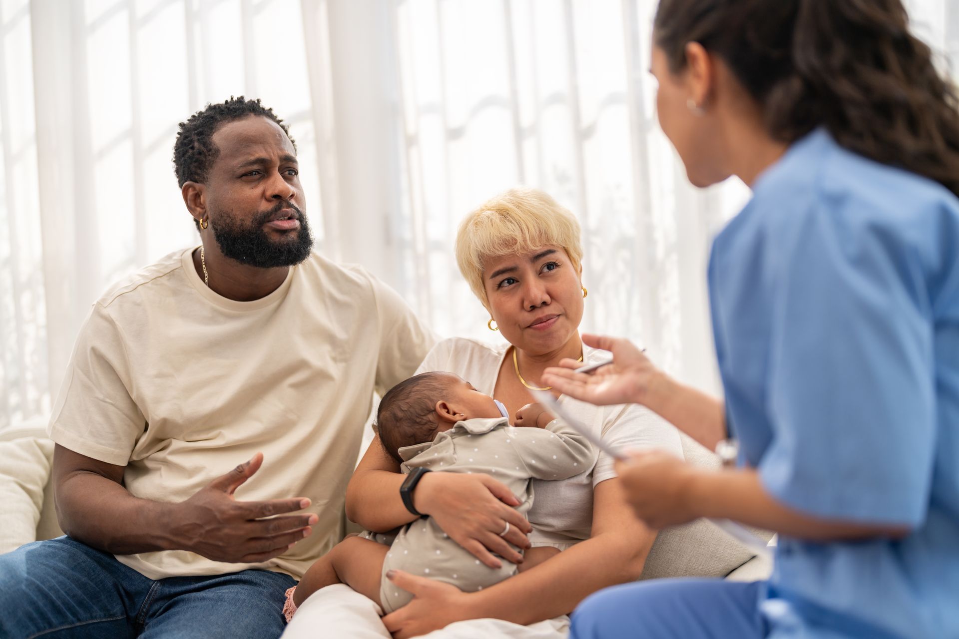 Une soignante discute avec un couple tenant un bébé dans une pièce lumineuse