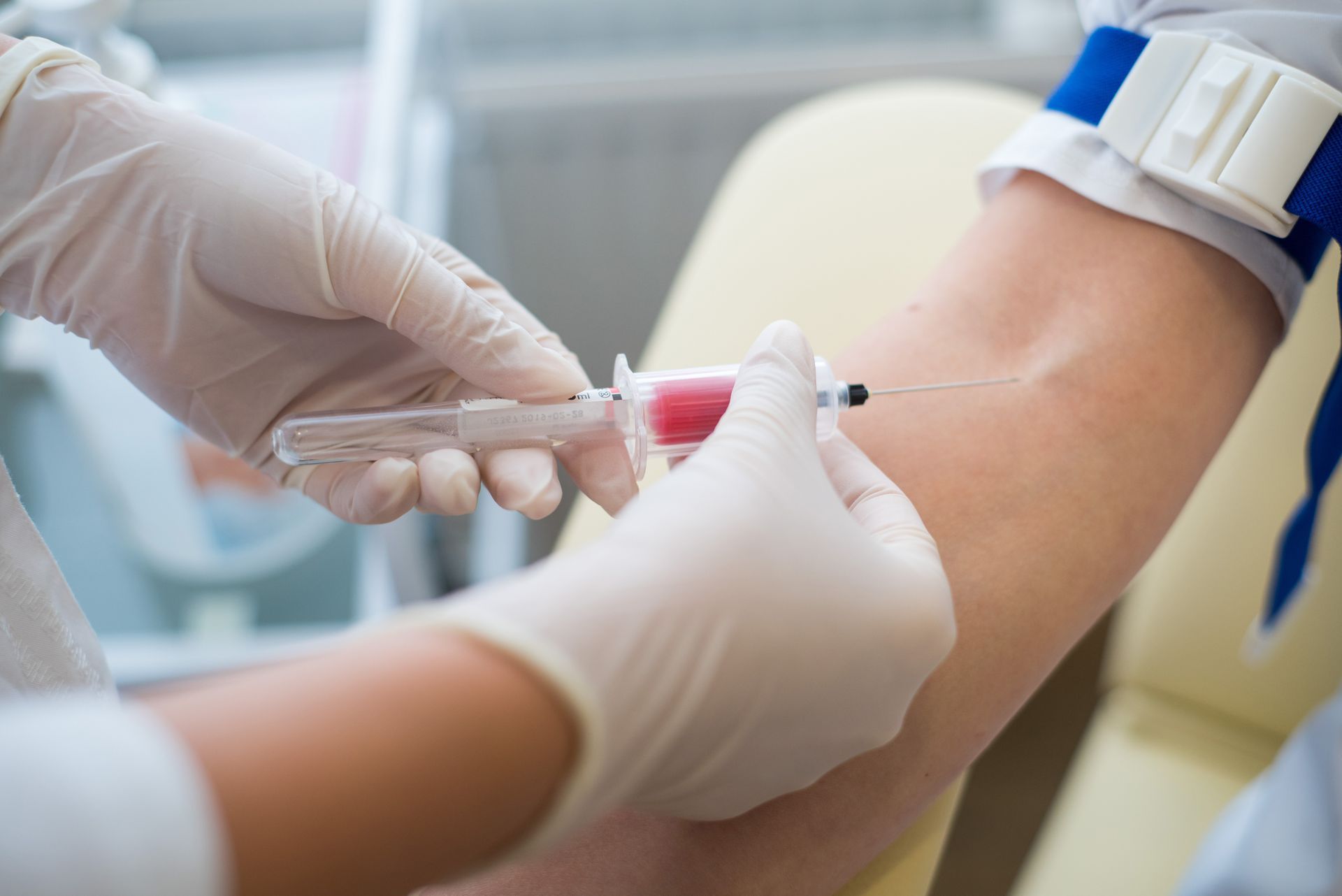 Un clinicien ganté prélève du sang au bras d'un patient à l'aide d'une seringue dans un environnement médical.