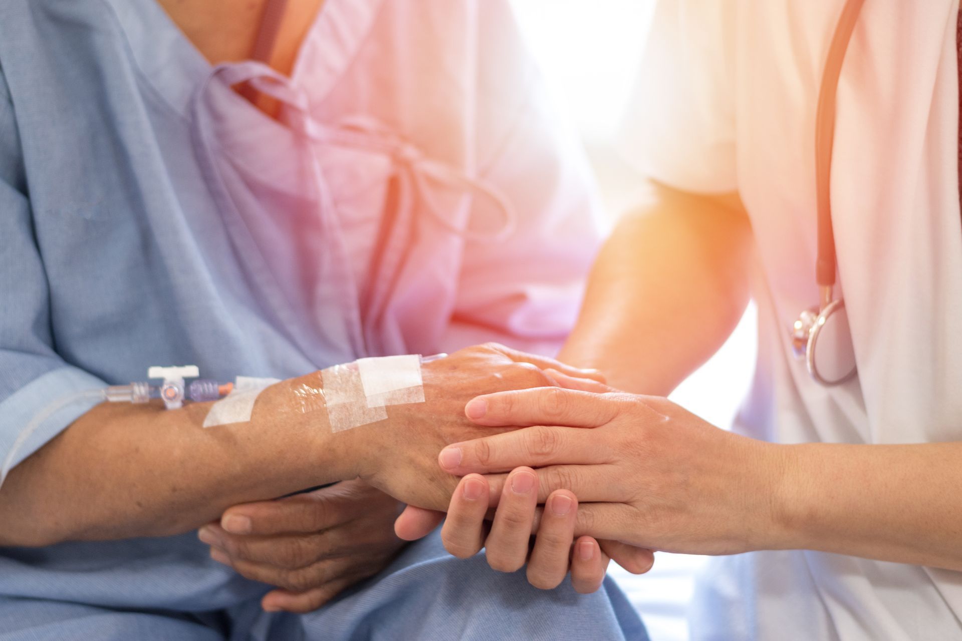 Un soignant tient la main d'un patient alité dans un hôpital, les pansements de la perfusion étant visibles.