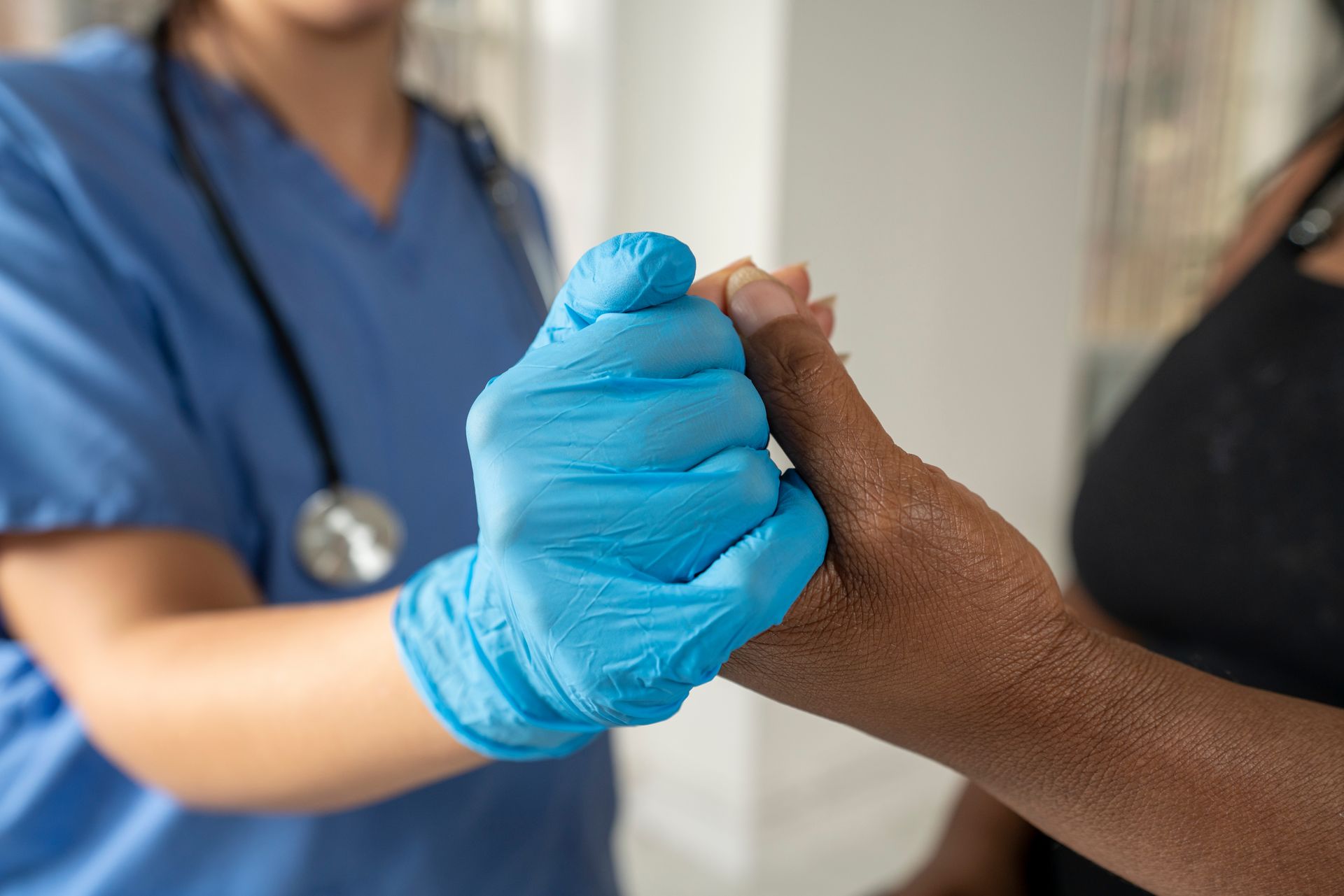 Un professionnel de la santé portant des gants bleus tient la main d'un patient dans un environnement clinique.