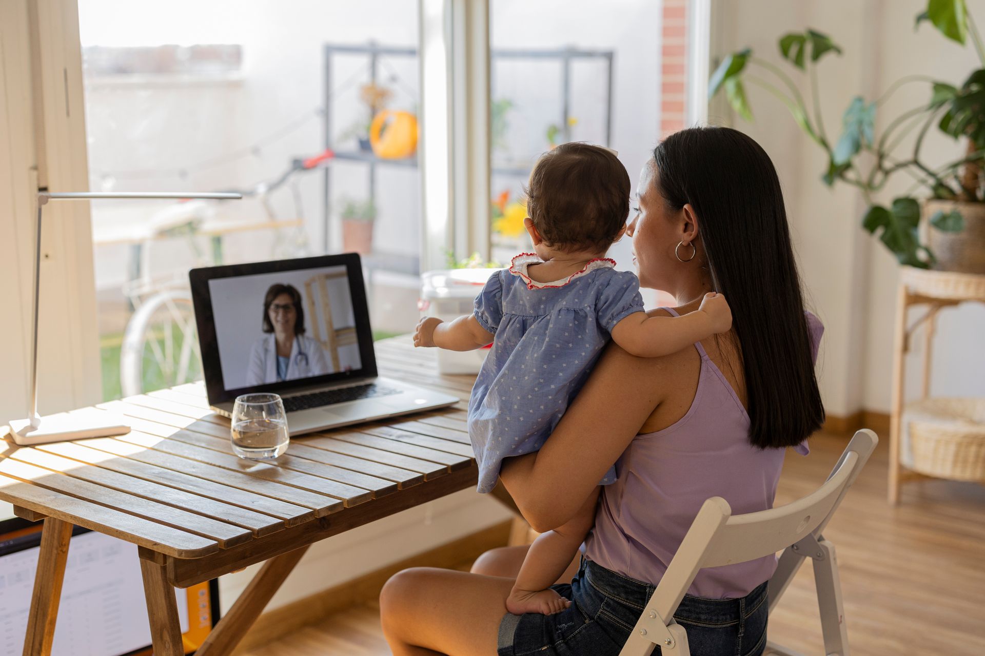 Une femme tenant un enfant lors d'un appel vidéo dans un bureau à domicile lumineux