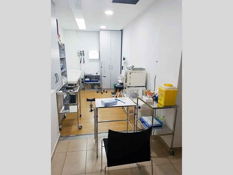 Sala de exploración médica con mesa de exploración blanca y equipamiento médico.