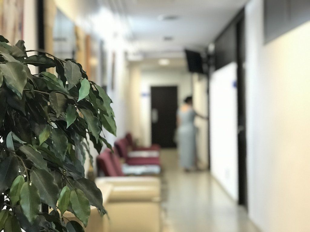 Pasillo con zona de espera y una persona vestida de azul claro cerca de una puerta.