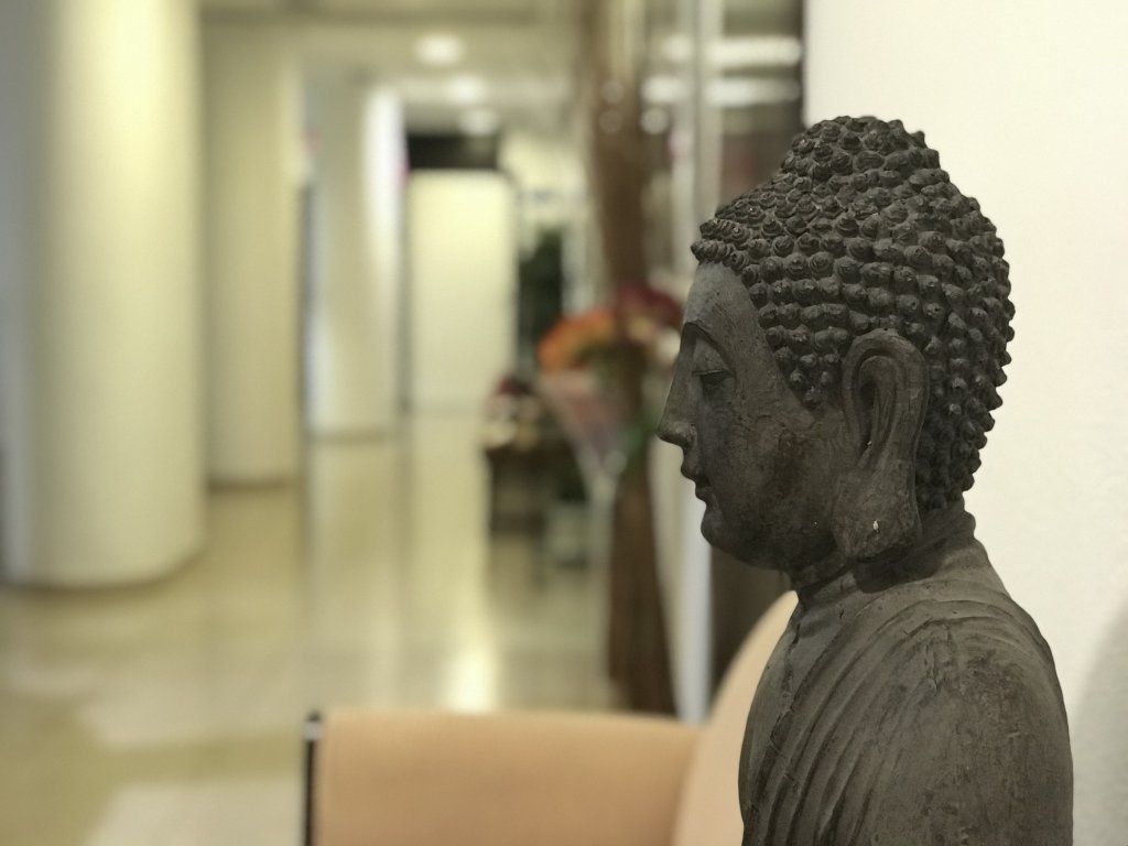 Estatua de Buda de piedra de perfil; fondo borroso de un pasillo.