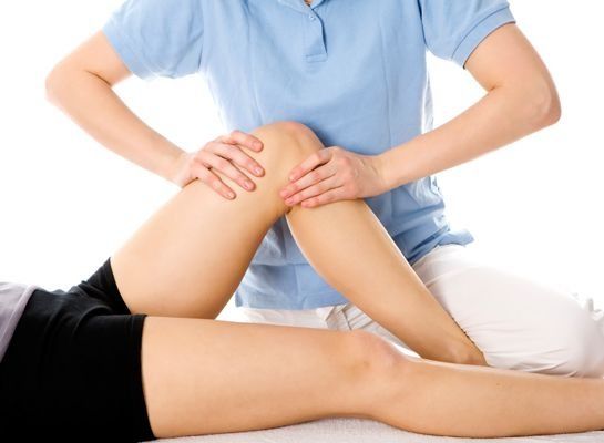 Terapeuta manipulando la rodilla del paciente. Camiseta azul claro, pantalón blanco. Fondo blanco.
