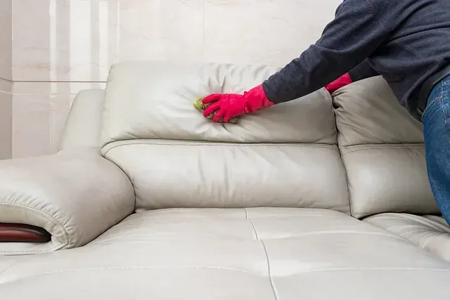 Una persona que lleva guantes rojos está limpiando un sofá de cuero blanco.
