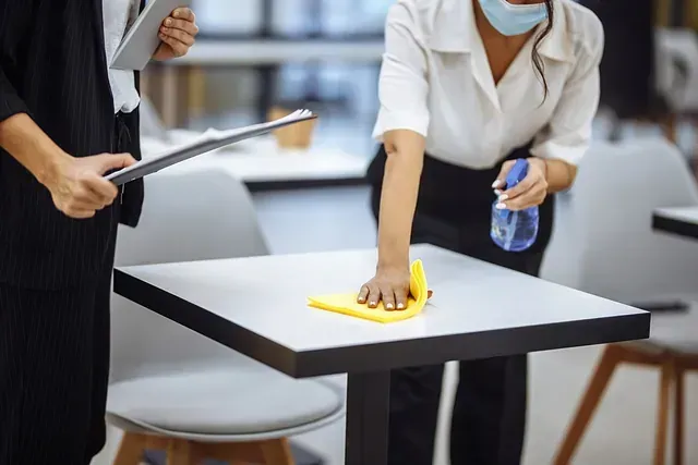 Una mujer que lleva una máscara está limpiando una mesa en un restaurante.