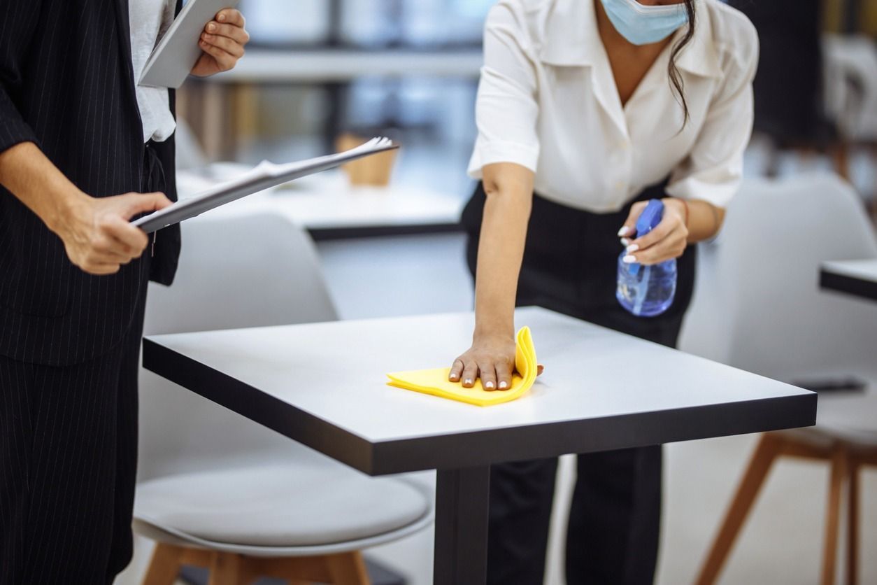 Una mujer que lleva una máscara está limpiando una mesa en un restaurante.