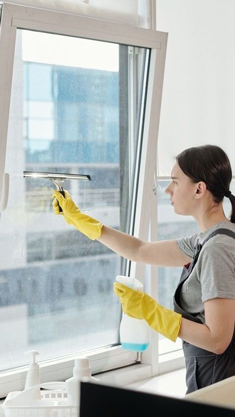 Una mujer con guantes amarillos está limpiando una ventana con una escobilla de goma.