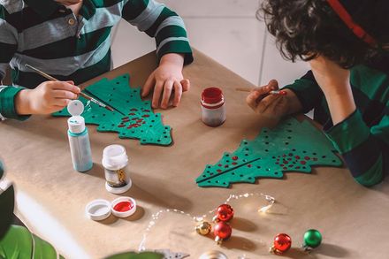 Zwei Kinder sitzen an einem Tisch und bemalen einen Weihnachtsbaum.