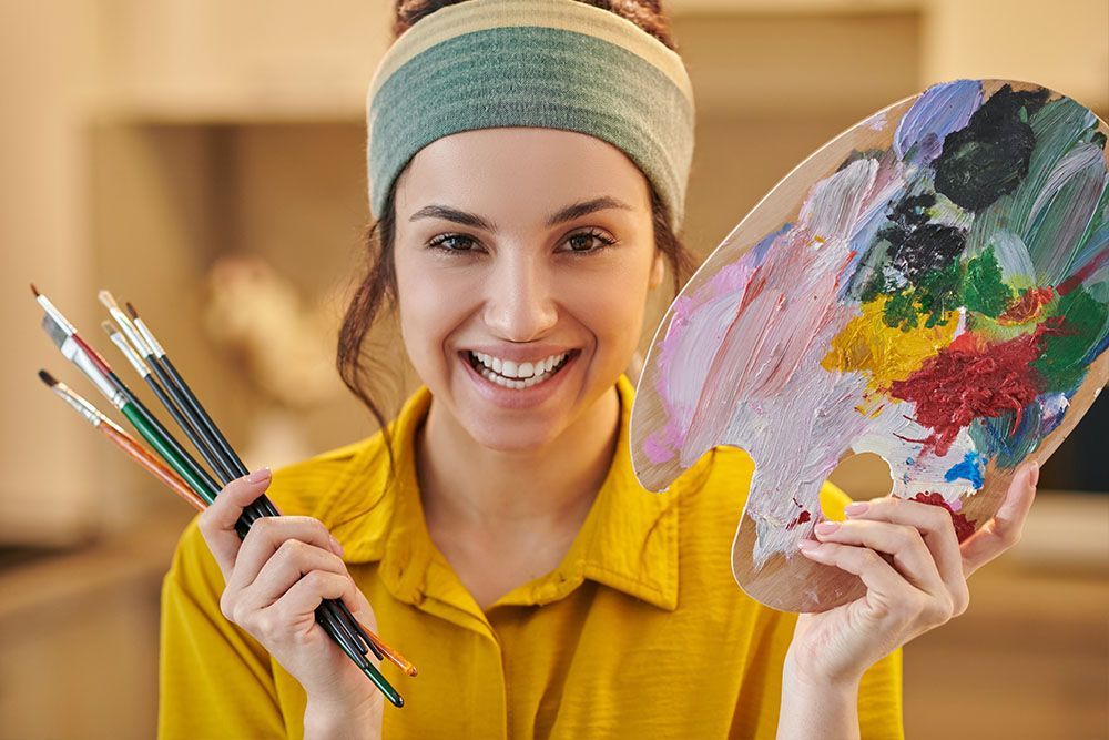Eine Frau hält eine Palette mit Farben und Pinseln.