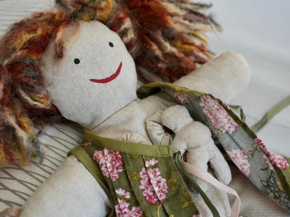 Una muñeca con cabello rojo sonríe y lleva un vestido floral.