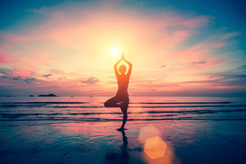 Una mujer está haciendo yoga en la playa al atardecer.
