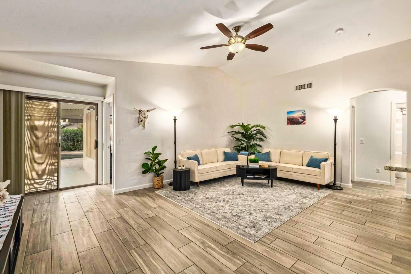 Bright living room with beige sectional, ceiling fan, rug, plants, and sliding glass doors