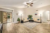 Bright living room with beige sectional, ceiling fan, rug, plants, and sliding glass doors
