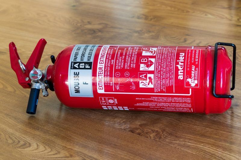 Extincteur rouge posé sur un plancher en bois, sa goupille et sa poignée visibles.