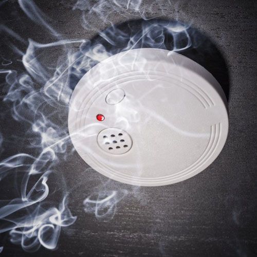 Détecteur de fumée blanc sur un plafond sombre, de la fumée tourbillonnant autour et un voyant rouge allumé
