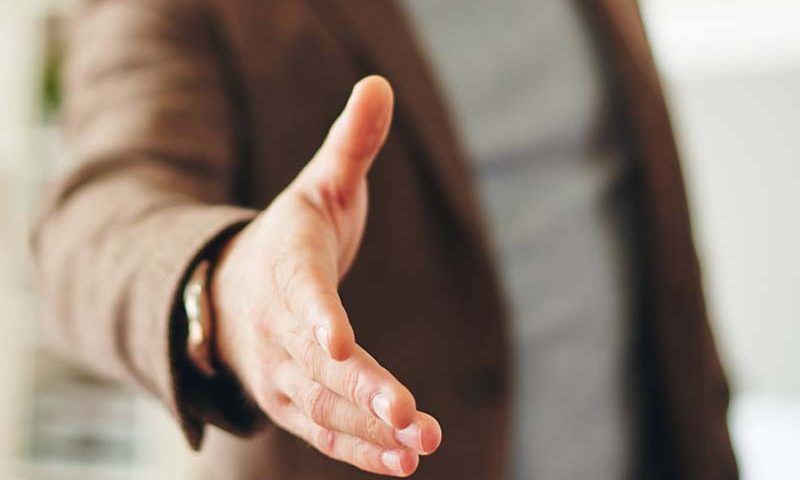 Main tendue dans une veste marron, offrant une poignée de main à l'intérieur