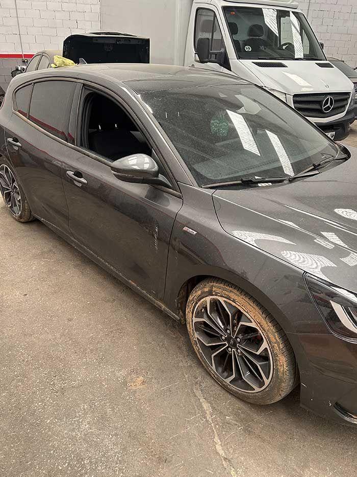 Un coche gris está aparcado en un estacionamiento al lado de una camioneta blanca.