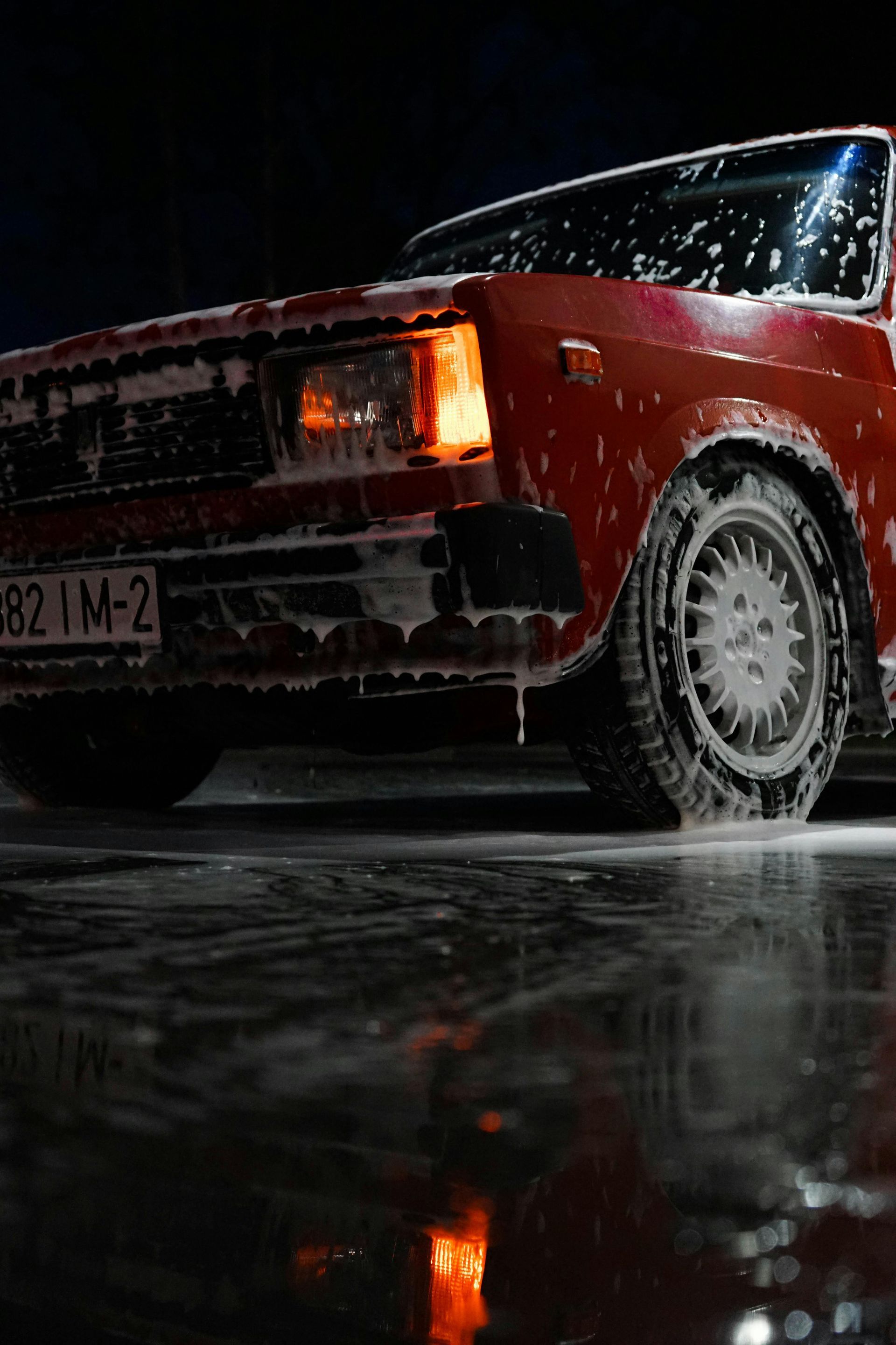 Un coche rojo circula por una carretera mojada por la noche.