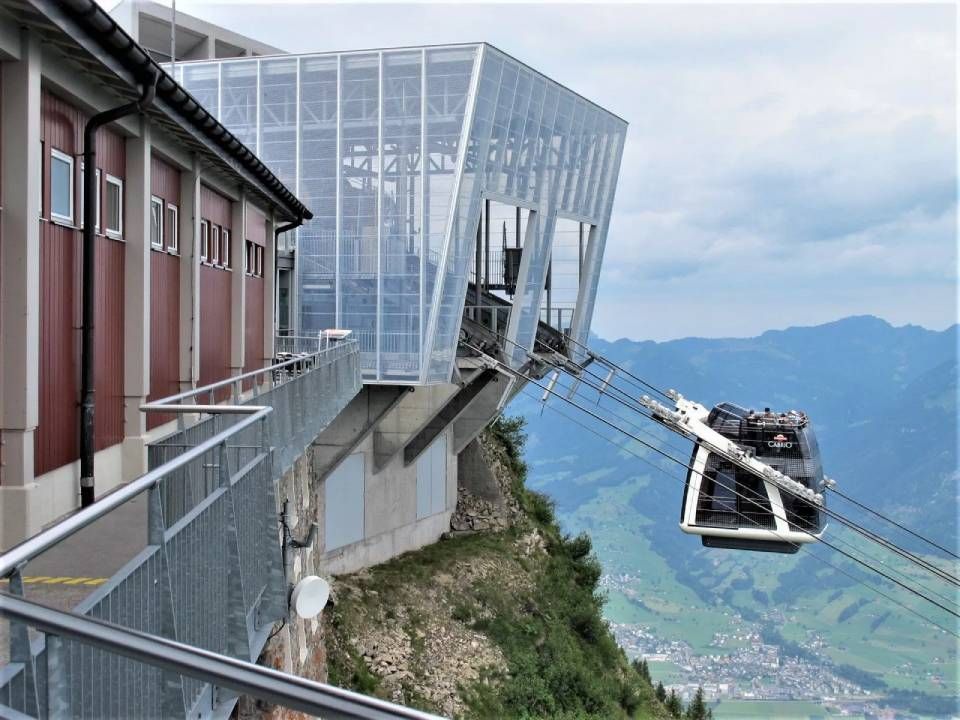 Eine Seilbahn erreicht eine moderne Bergstation, im Hintergrund ist eine malerische Tallandschaft zu sehen.