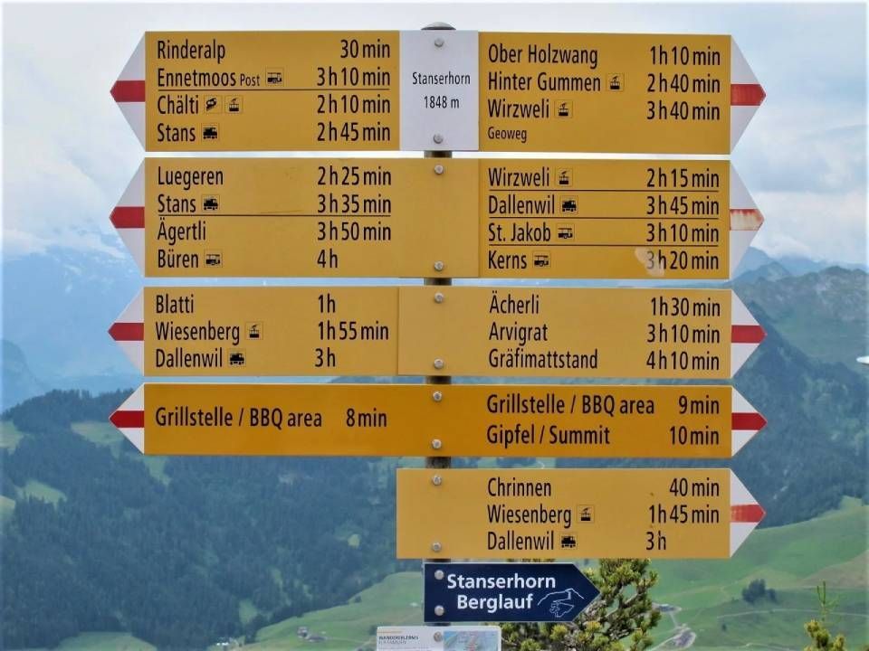 Ein gelber Wanderwegweiser am Stanserhorn listet Ziele und Gehzeiten in einer malerischen alpinen Umgebung auf.