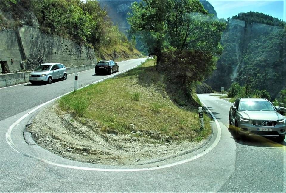 Eine scharfe Haarnadelkurve auf einer Bergstrasse, auf der tagsüber Autos in beide Richtungen fahren.