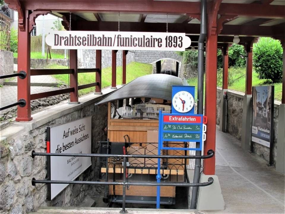 Die hölzerne Standseilbahnkabine an der Station der Drahtseilbahn in der Schweiz, mit einem Schild mit der Jahreszahl 1893 und einer Uhr.